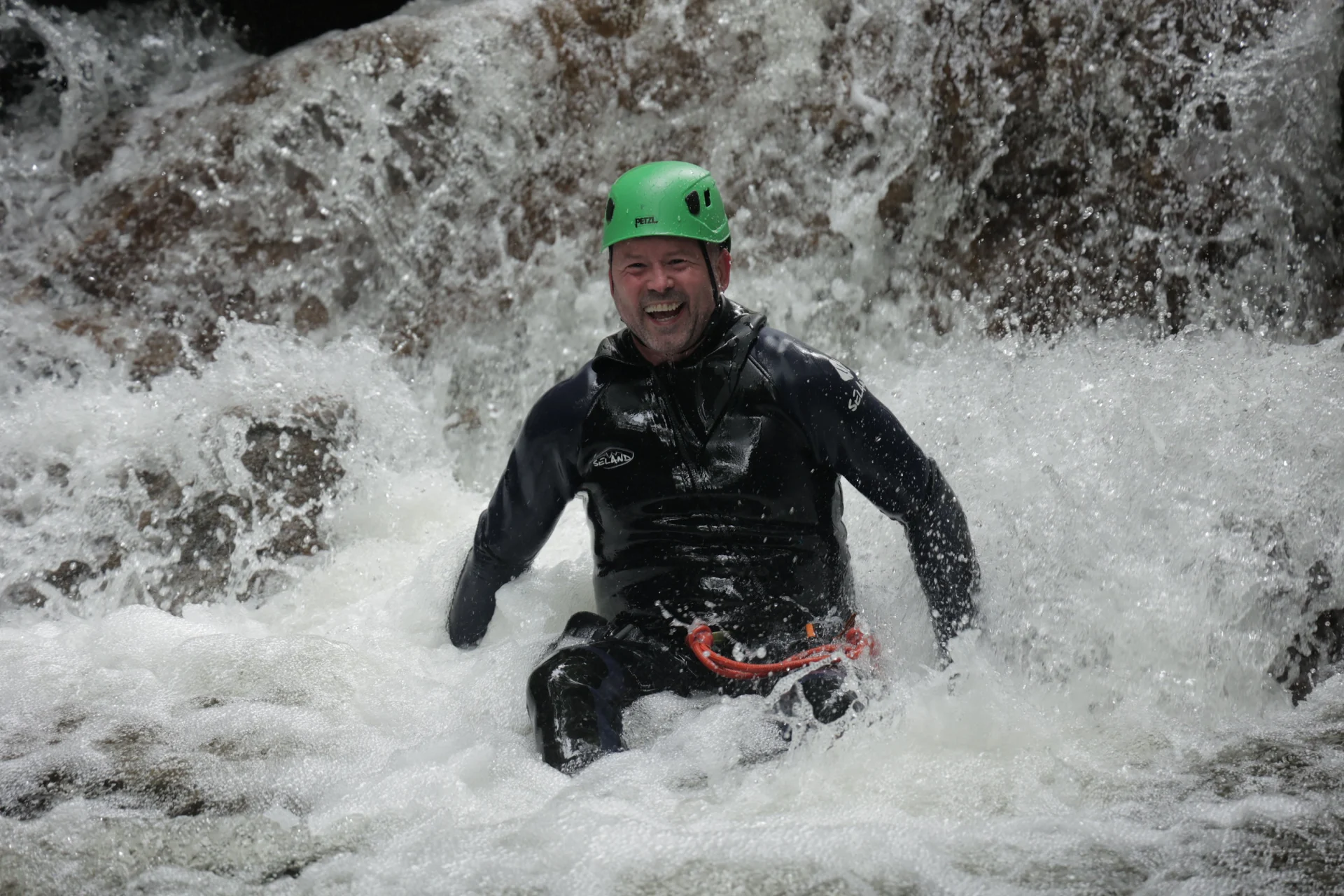 A man laughing as he splashes in the water of the Falls of Bruar on a Canyoning trip.